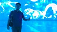 Seorang pria berpartisipasi dalam sesi olahraga laser indoor dengan latar belakang proyeksi visual dinamis