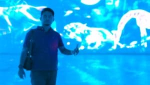 Seorang pria berpartisipasi dalam sesi olahraga laser indoor dengan latar belakang proyeksi visual dinamis