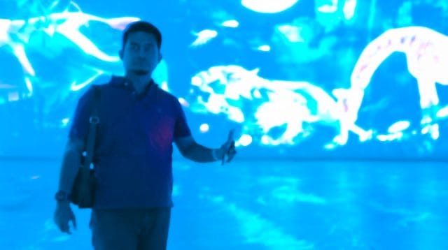 Seorang pria berpartisipasi dalam sesi olahraga laser indoor dengan latar belakang proyeksi visual dinamis
