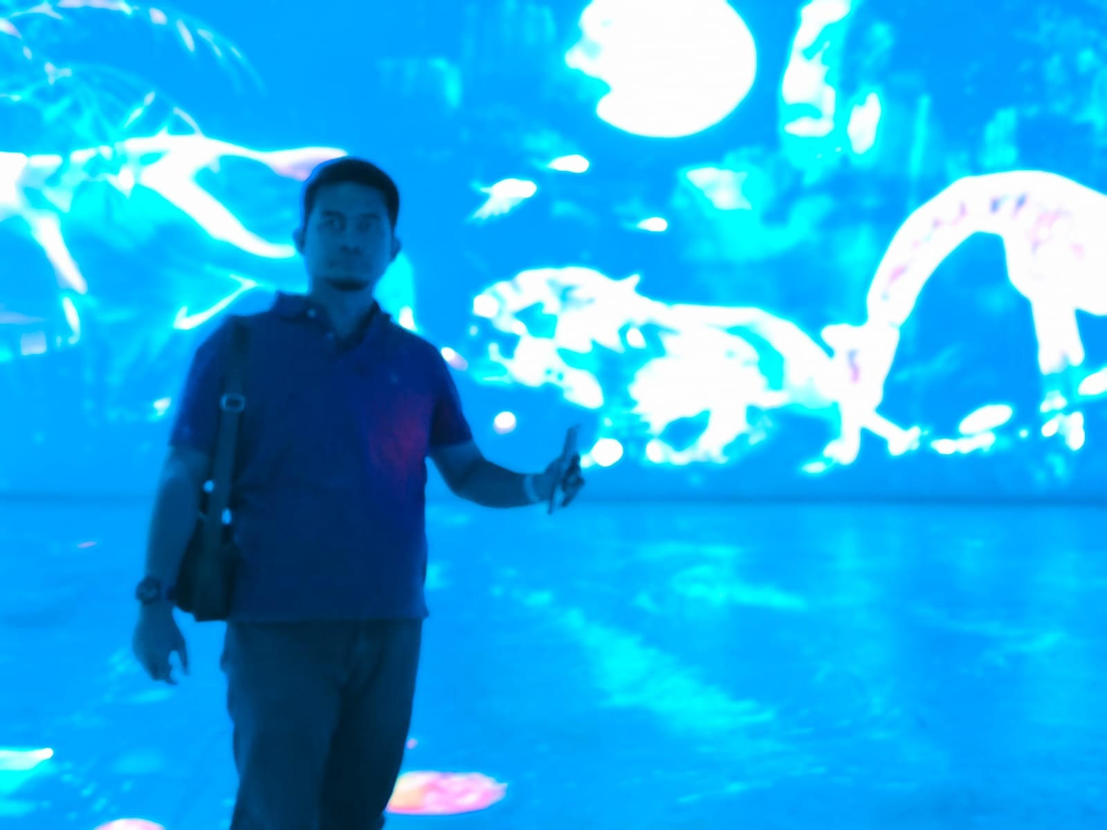 Seorang pria berpartisipasi dalam sesi olahraga laser indoor dengan latar belakang proyeksi visual dinamis