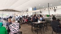 Suasana warung kopi modern yang ramai oleh pengunjung yang menerapkan budaya kerja fleksibel dengan laptop