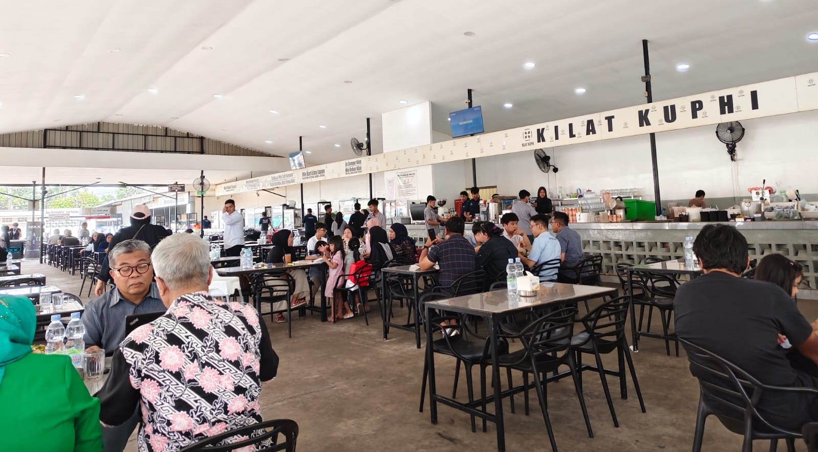 Suasana warung kopi modern yang ramai oleh pengunjung yang menerapkan budaya kerja fleksibel dengan laptop