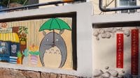 Lukisan mural karakter animasi Totoro memegang payung hijau di tembok jalanan Qingdao