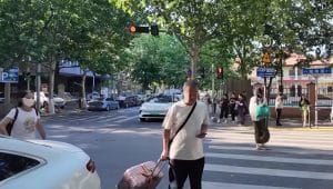 Seorang turis pria membawa koper besar menyeberangi jalan raya dengan aman di kota Qingdao