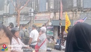 Seorang turis mancanegara berjalan kaki melewati dekorasi durian raksasa di trotoar Armenian Street