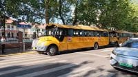 Bus sekolah berwarna kuning cerah khas Qingdao sedang melintasi area penyeberangan jalan.