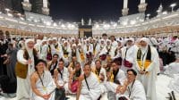 Rombongan jamaah umrah Indonesia berkumpul dengan latar belakang Kakbah di pelataran Masjidil Haram yang dipadati lautan manusia