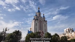 Gereja Dormition di Khabarovsk yang menjulang tinggi dengan ciri khas kubah emas dan biru, dikelilingi pepohonan hijau.