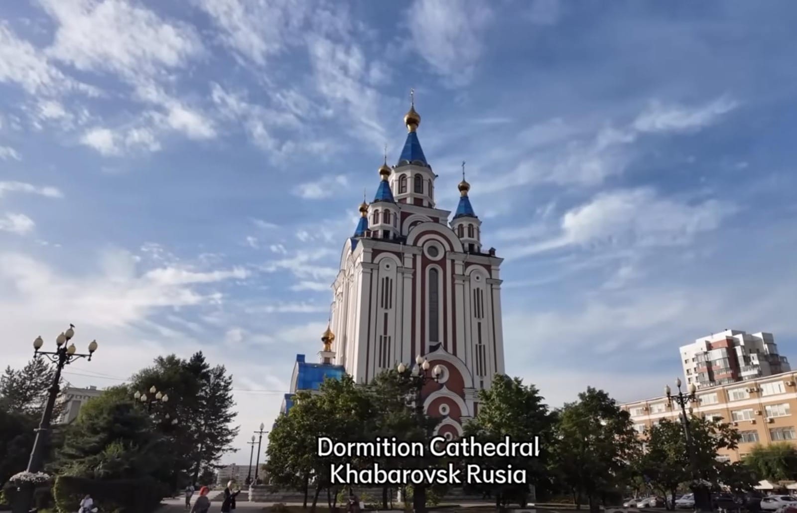 Gereja Dormition di Khabarovsk yang menjulang tinggi dengan ciri khas kubah emas dan biru, dikelilingi pepohonan hijau.