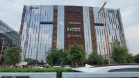 Fasad megah gedung perkantoran kaca bertingkat tinggi di kawasan pusat bisnis Gurugram yang menampilkan papan nama berbagai merek perusahaan multinasional terkemuka