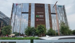 Fasad megah gedung perkantoran kaca bertingkat tinggi di kawasan pusat bisnis Gurugram yang menampilkan papan nama berbagai merek perusahaan multinasional terkemuka