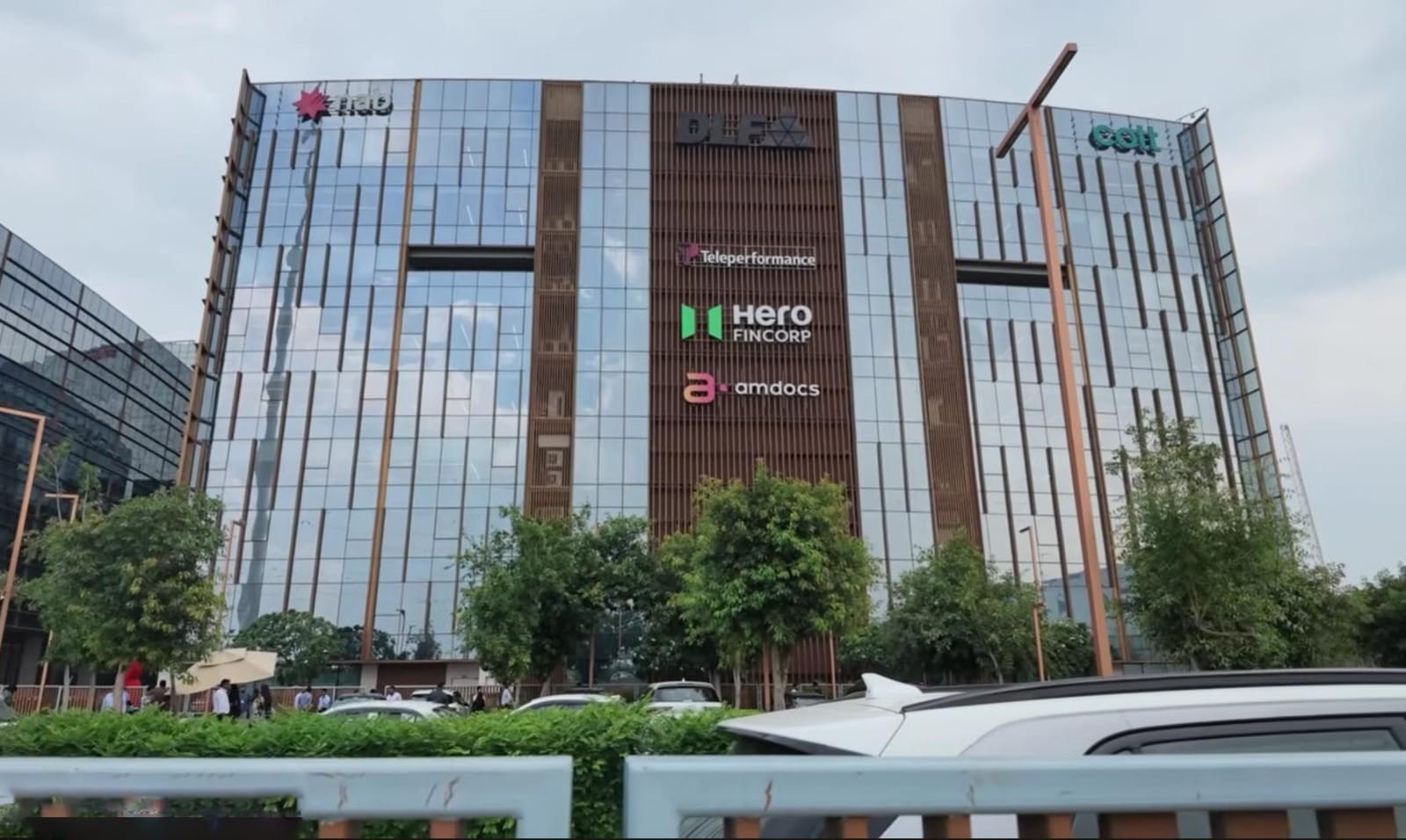 Fasad megah gedung perkantoran kaca bertingkat tinggi di kawasan pusat bisnis Gurugram yang menampilkan papan nama berbagai merek perusahaan multinasional terkemuka