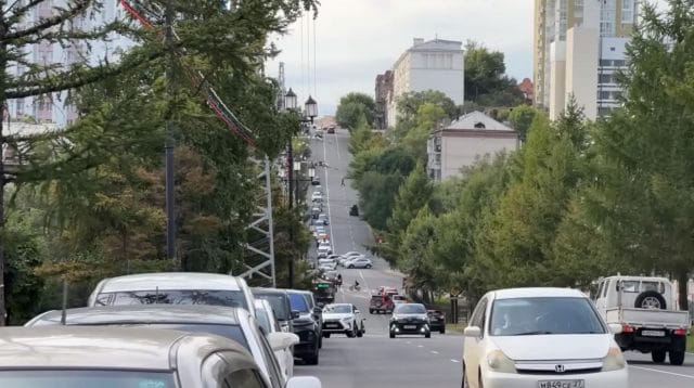 Arus kendaraan dan pejalan kaki di jalanan kota Khabarovsk yang tertib dengan latar perpaduan arsitektur klasik dan modern.