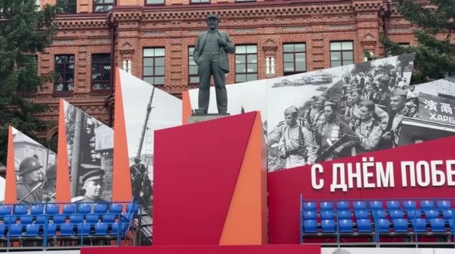 Patung monumen tokoh revolusioner Vladimir Lenin yang berdiri kokoh dengan dekorasi peringatan sejarah di belakangnya.