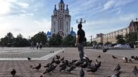 Sekawanan burung merpati beterbangan bebas di pelataran gereja di Khabarovsk dengan latar bangunan gereja Ortodoks.