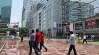 Para pekerja dan pengunjung sedang berjalan bersantai melintasi pelataran komersial modern Cyber Hub di Gurugram dengan latar belakang gedung-gedung perkantoran.