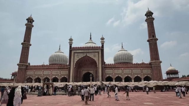 Kemegahan bangunan utama Jama Masjid Delhi peninggalan Shah Jahan dengan kubah marmer putih dan menara batu pasir merah yang dipadati lautan jamaah di halamannya.