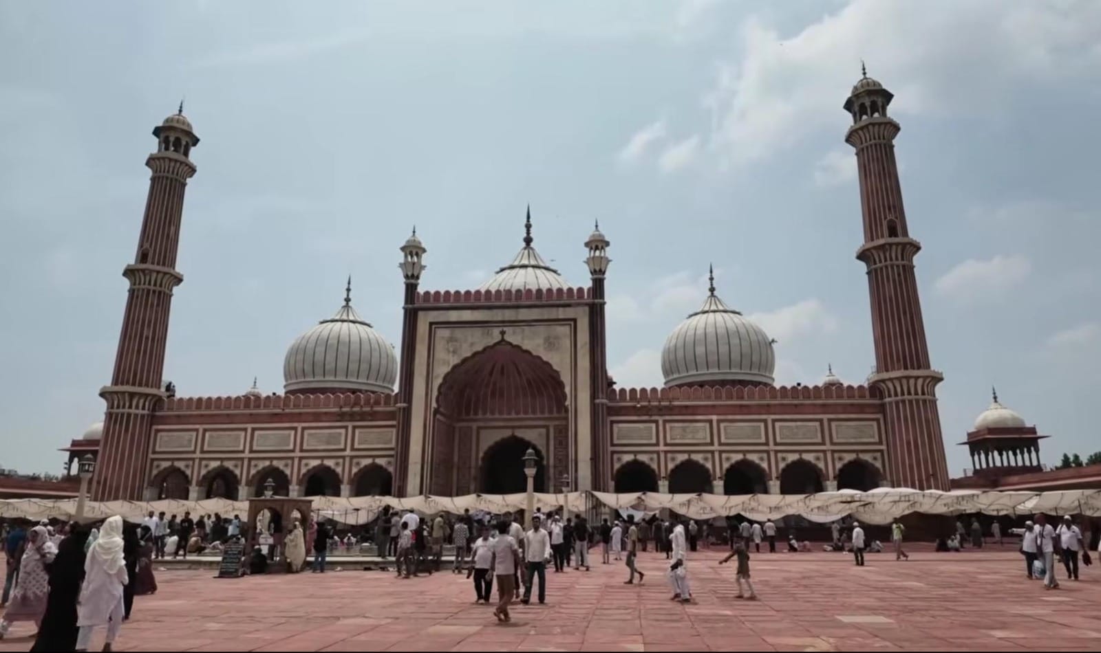 Kemegahan bangunan utama Jama Masjid Delhi peninggalan Shah Jahan dengan kubah marmer putih dan menara batu pasir merah yang dipadati lautan jamaah di halamannya.