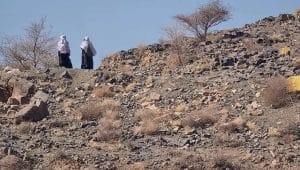 Dua perempuan berdiri di atas bukit bebatuan yang tandus dan gersang di kawasan Bani Sa’ad