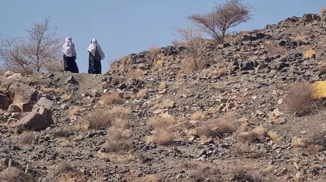 Dua perempuan berdiri di atas bukit bebatuan yang tandus dan gersang di kawasan Bani Sa’ad