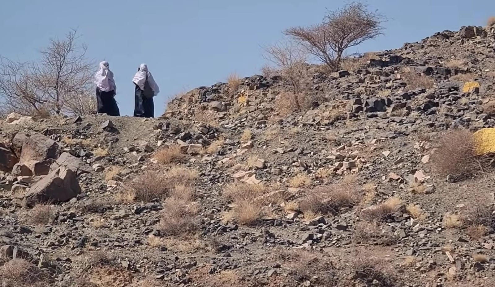 Dua perempuan berdiri di atas bukit bebatuan yang tandus dan gersang di kawasan Bani Sa’ad