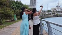 Dua remaja perempuan Sri Lanka sedang asyik berswafoto di tepi perairan kota.