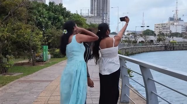 Dua remaja perempuan Sri Lanka sedang asyik berswafoto di tepi perairan kota.