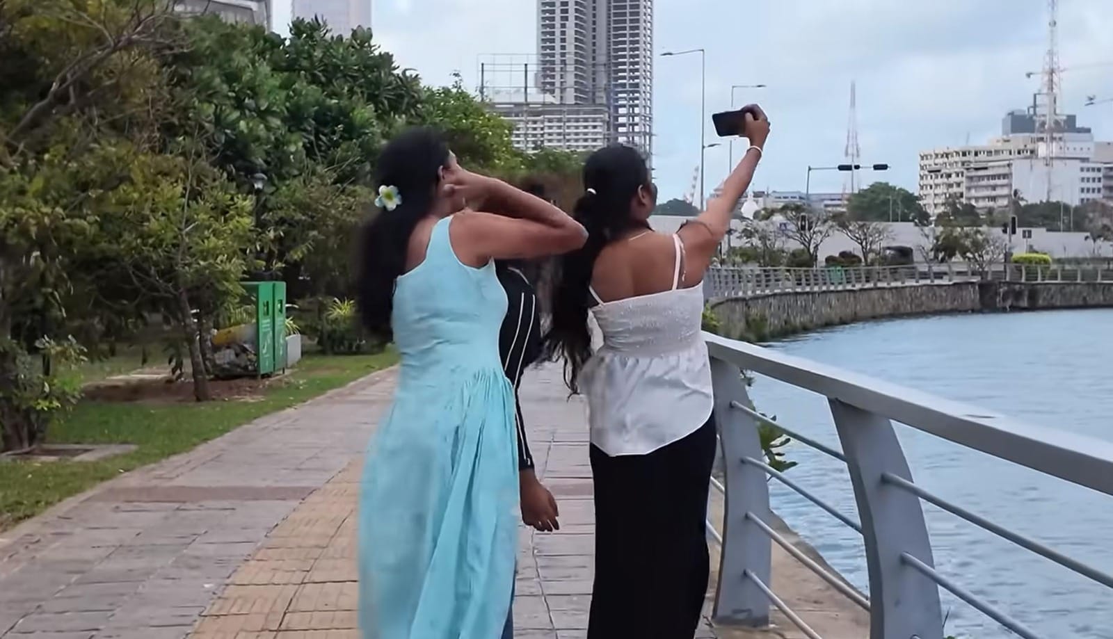 Dua remaja perempuan Sri Lanka sedang asyik berswafoto di tepi perairan kota.