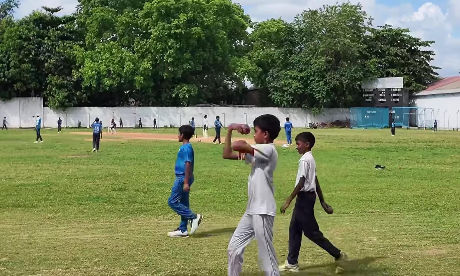 Anak-Anak Berlatih Kriket di Sri Lanka Sekelompok anak bermain kriket di tanah lapang berumput hijau.