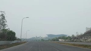 Jalan raya lebar di kawasan IKN yang diselimuti kabut asap pekat, membuat bangunan di kejauhan tampak samar