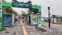 Papan gerbang hijau bertuliskan Nusantara Park di kawasan komersial modern dengan deretan tenant kontainer.
