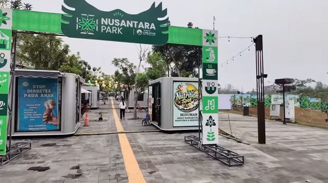 Papan gerbang hijau bertuliskan Nusantara Park di kawasan komersial modern dengan deretan tenant kontainer.