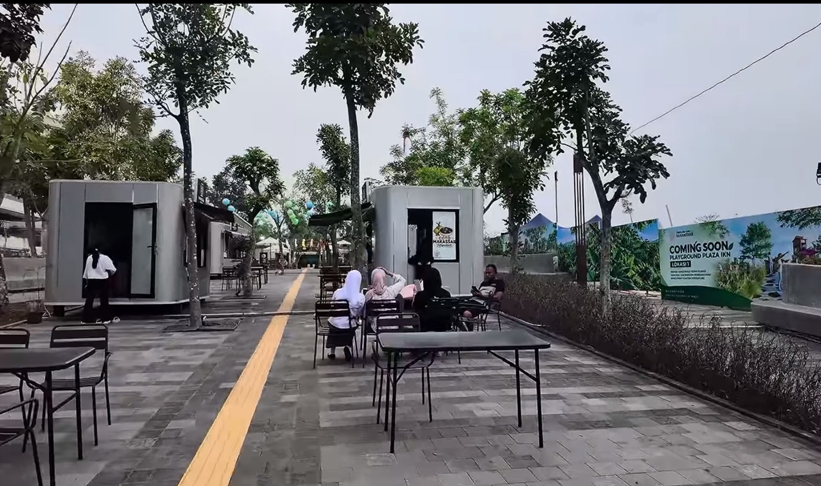 Sekelompok orang duduk santai menikmati waktu di area kafe terbuka bernuansa modern.