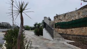 Tangga beton eksterior berpegangan besi di area fasilitas publik dengan dinding batu alam estetis.
