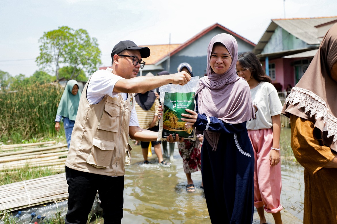Petugas BAZNAS menyalurkan bantuan beras Zakat Fitrah kepada warga di daerah banjir.