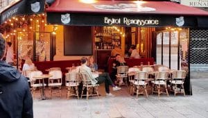 Suasana luar ruangan sebuah kafe kecil di Paris bernama Bistrot Renaissance dengan beberapa pelanggan duduk di kursi rotan.
