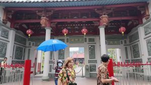 Pengunjung memegang payung biru berdiri di depan gerbang Vihara Satya Budhi Bandung yang megah.