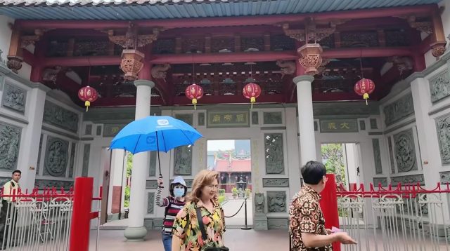 Pengunjung memegang payung biru berdiri di depan gerbang Vihara Satya Budhi Bandung yang megah.