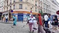 Suasana jalanan kota Paris yang dipenuhi pejalan kaki dengan latar belakang bangunan apartemen berarsitektur klasik.