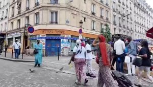 Suasana jalanan kota Paris yang dipenuhi pejalan kaki dengan latar belakang bangunan apartemen berarsitektur klasik.