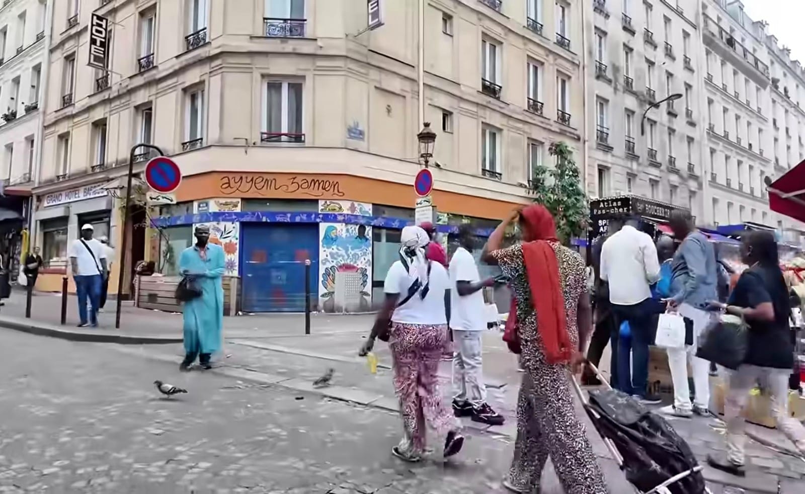 Suasana jalanan kota Paris yang dipenuhi pejalan kaki dengan latar belakang bangunan apartemen berarsitektur klasik.