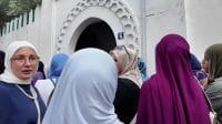 Sekelompok perempuan Muslim berhijab berkumpul di depan pintu masuk bangunan bercat putih dengan ornamen khas.