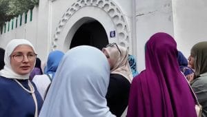 Sekelompok perempuan Muslim berhijab berkumpul di depan pintu masuk bangunan bercat putih dengan ornamen khas.